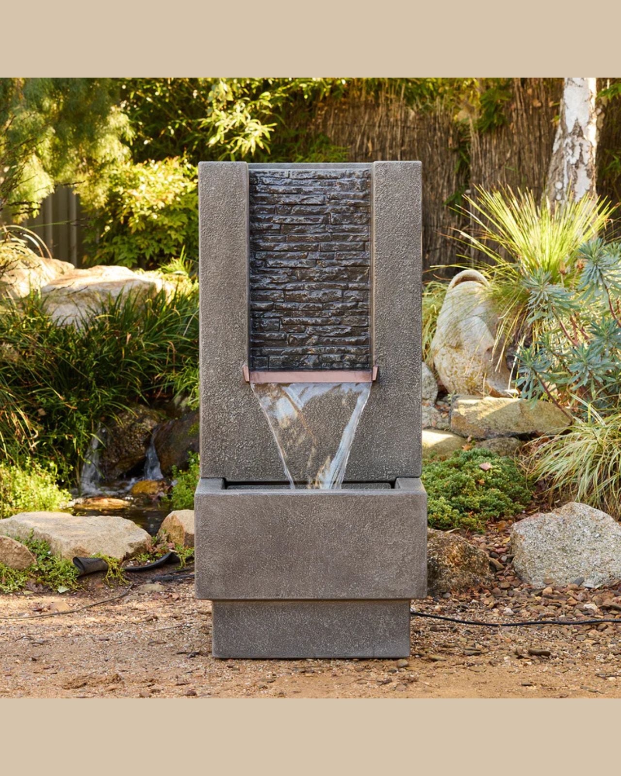 Outdoor water fountain in a garden setting with rocks and plants.