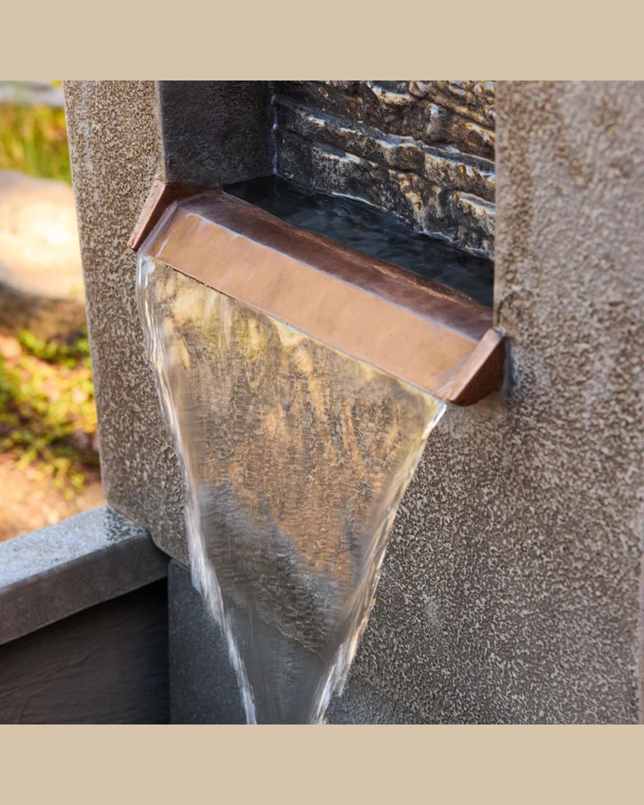 Water flowing from a stone fountain with a copper edge.