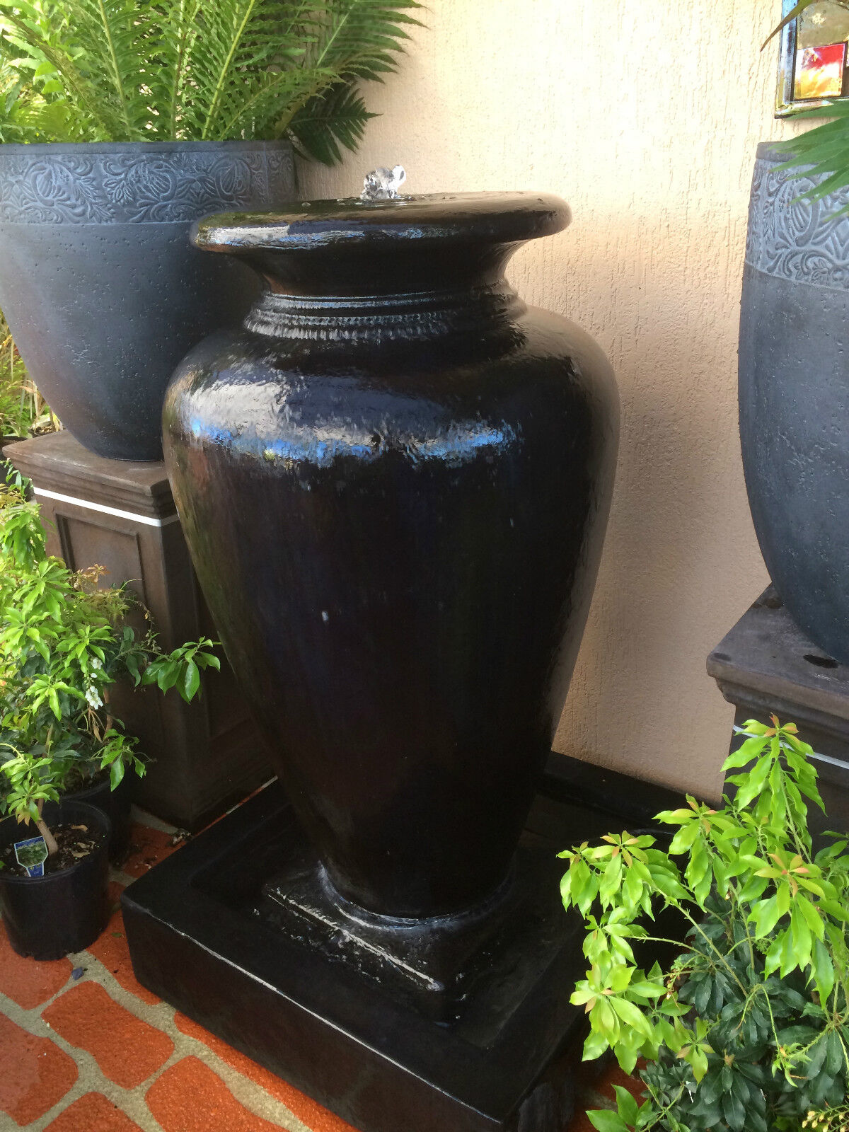 A black modern cascading urn water feature made of Glass Reinforced Concrete, placed on a base.