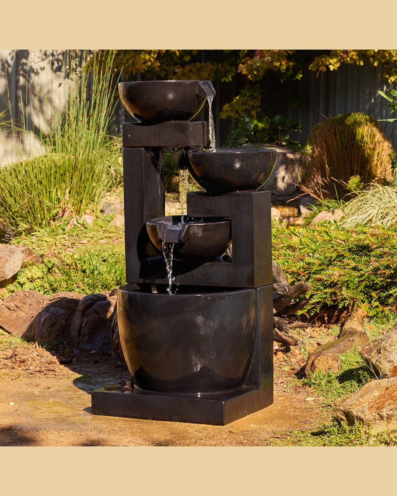 Outdoor cascading water fountain with three-tiered bowl design in a garden setting.