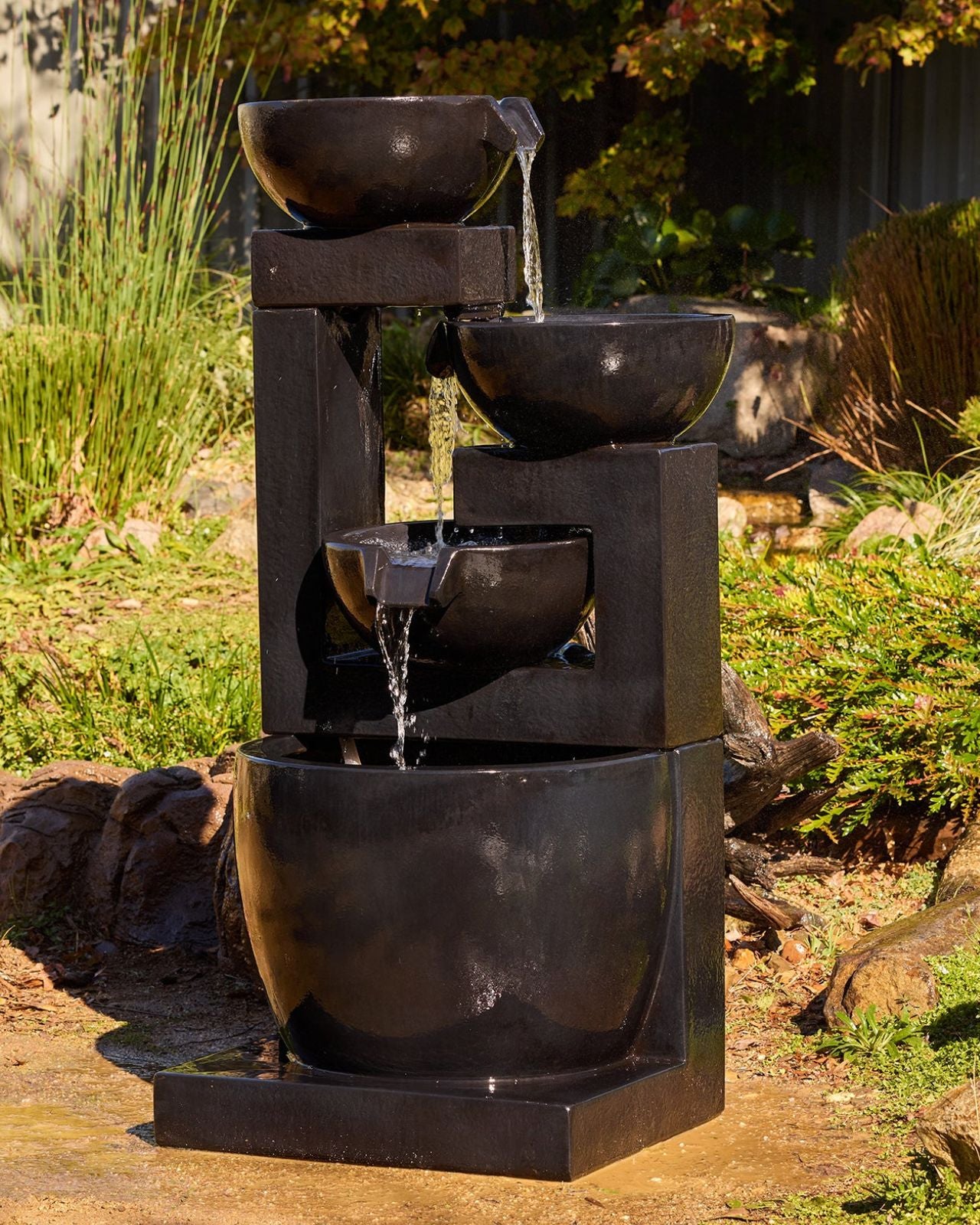 Outdoor tiered cascading water fountain with three bowls in a garden setting