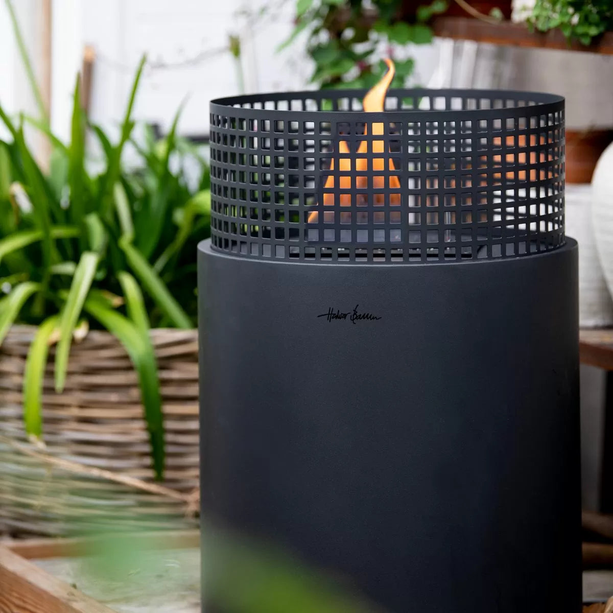 A matte black outdoor tenderflame fire pit with a cylindrical body and a top mesh screen.