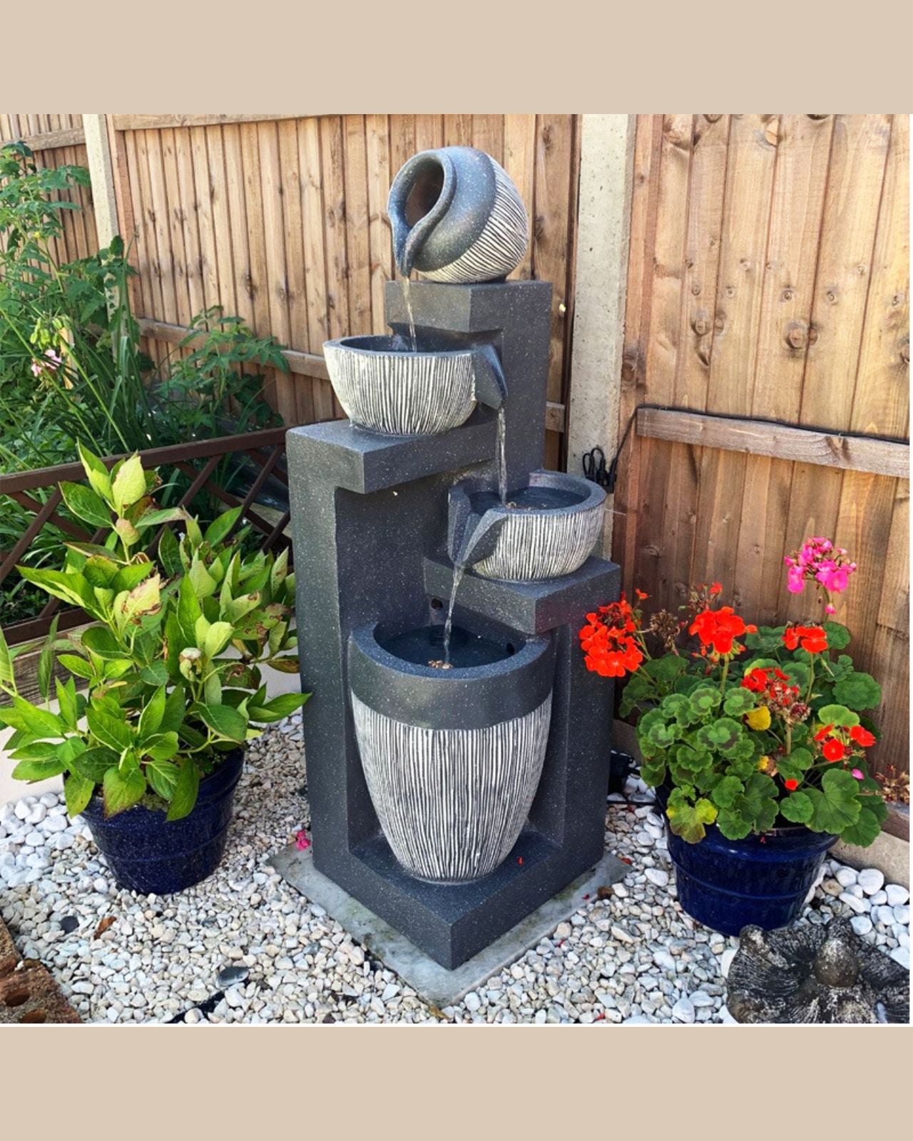 Outdoor garden water feature with a tiered cascading structure and potted plants.