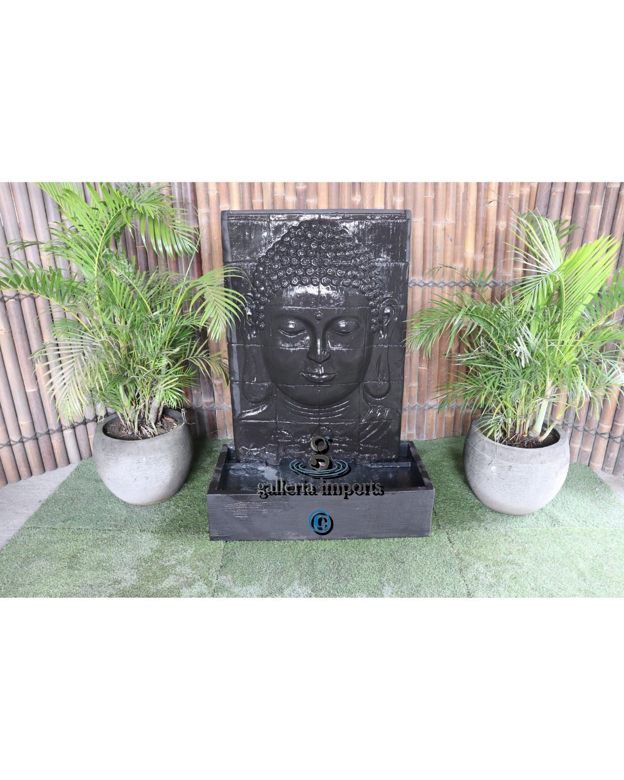 Fountain with Buddha face design in a garden setting with plants and a wooden fence.