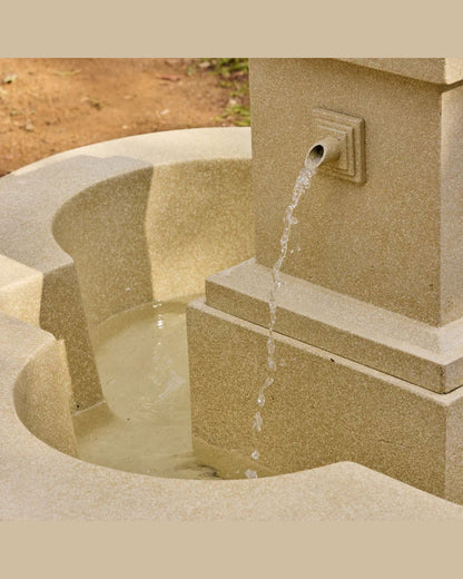 Stone fountain with water flowing into a basin on a beige background