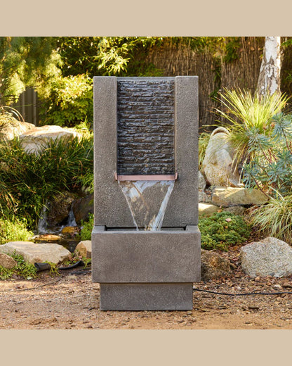 Outdoor water fountain in a garden setting with rocks and plants.