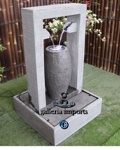 Decorative water fountain with a cylindrical stone-like design on a grassy surface.