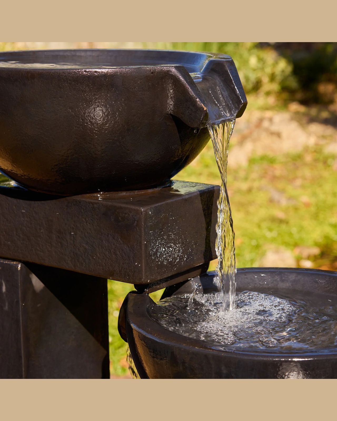 Black outdoor water fountain with water flowing into a basin.