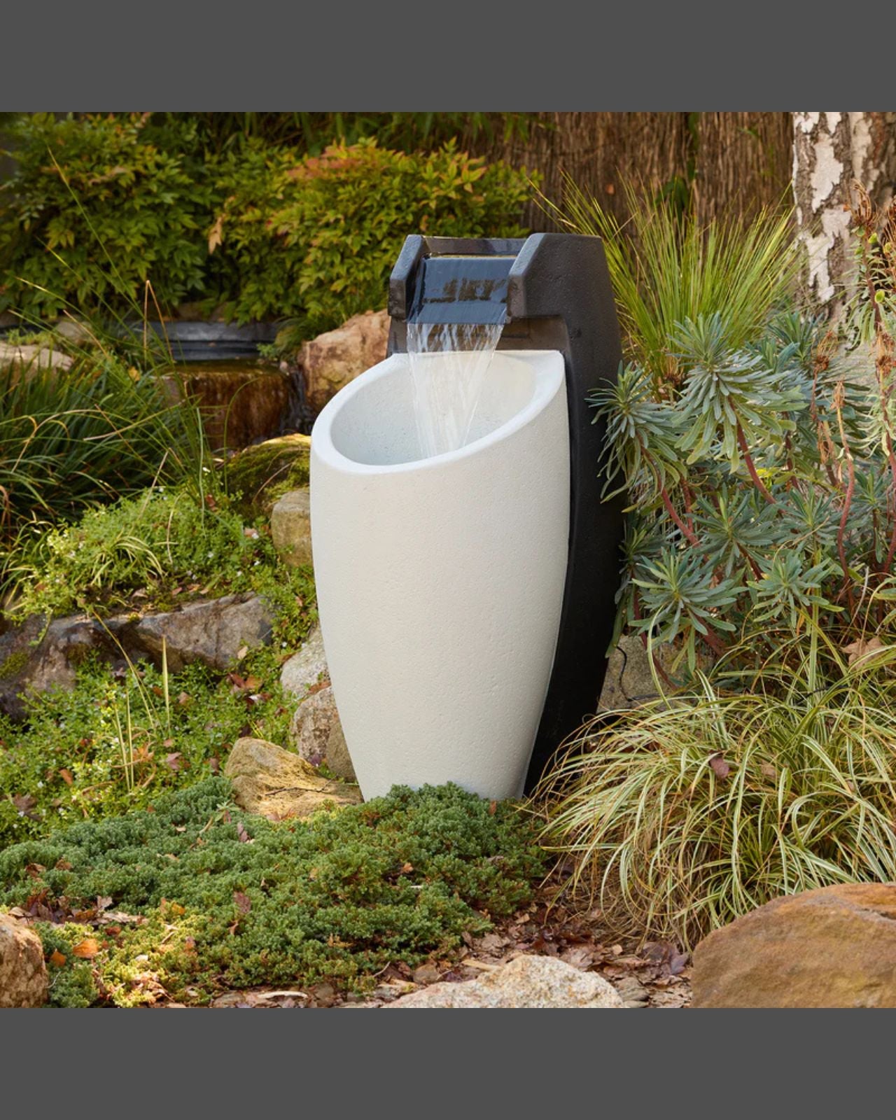 White Aegea outdoor fountain with black pump surrounded by greenery