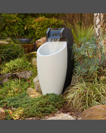 White Aegea outdoor fountain with black pump surrounded by greenery