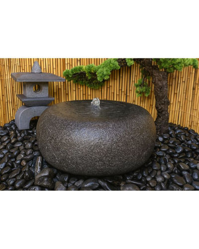 Decorative stone water feature in a garden setting with a bamboo fence and tree.