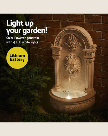 Decorative lion head water fountain with solar and LED lights against a brick wall.