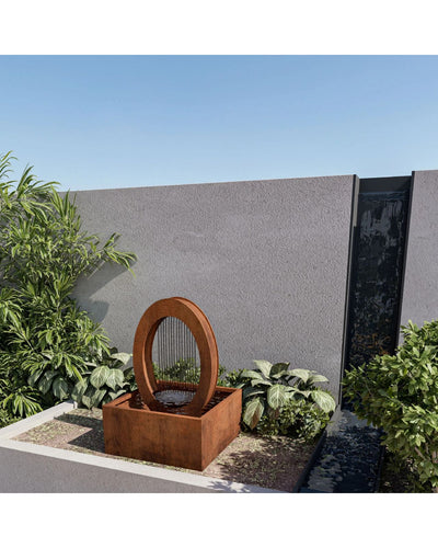 Rust-colored outdoor water fountain with circular design in a garden setting.