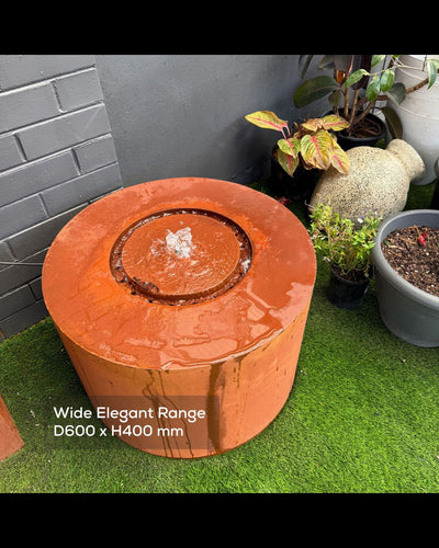 Round terracotta-colored outdoor corten steel feature with plants and a gray wall in the background