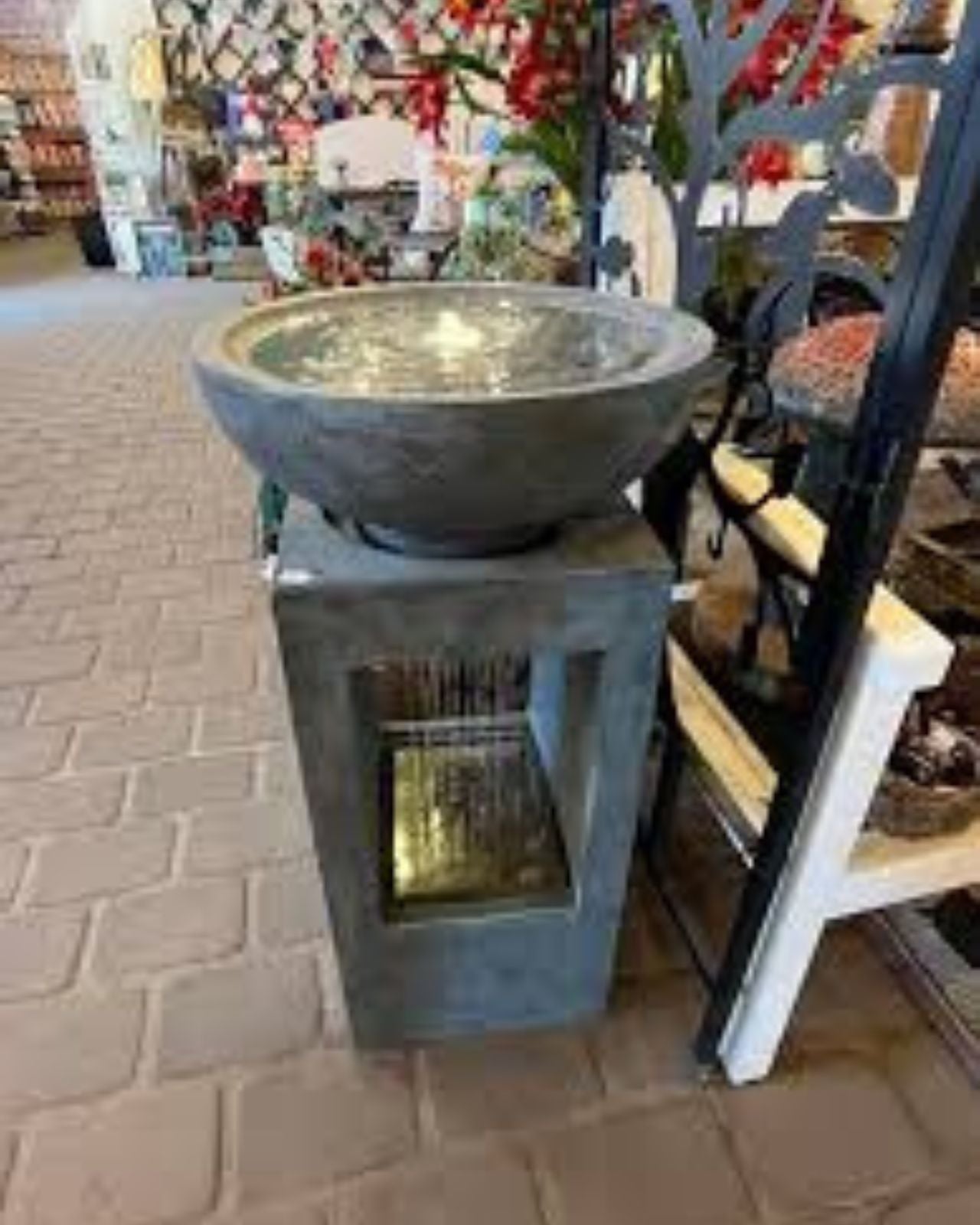 Decorative stone bowl water feature on a pedestal in an indoor setting with chairs and a table in the background.