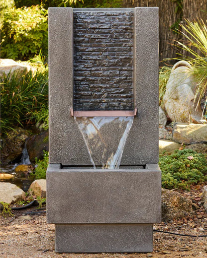 Decorative stone water fountain in a garden setting with plants and rocks.