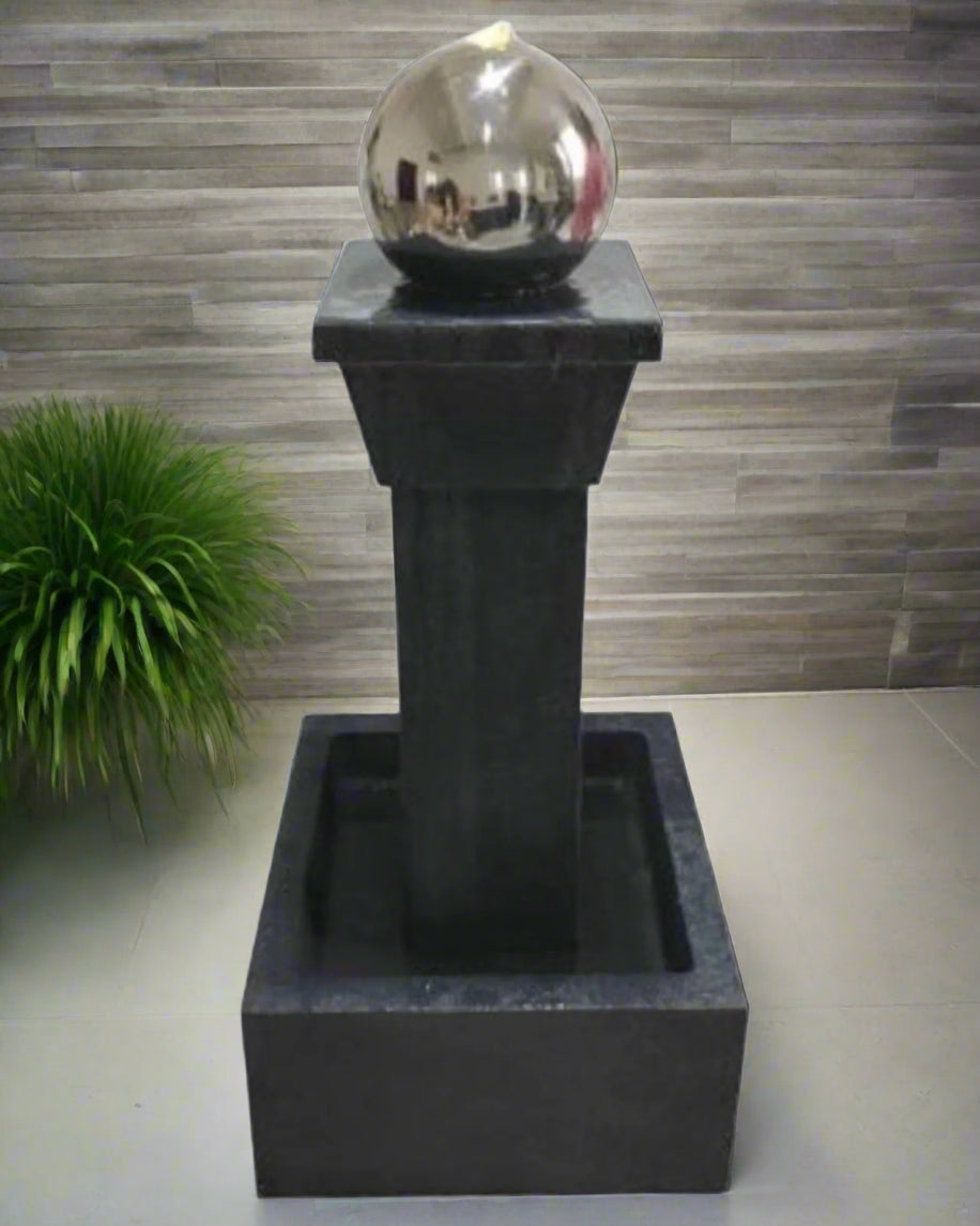 Black pedestal water fountain with a silver spherical object placed indoors