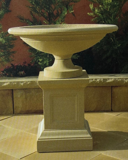 Decorative concrete water fountain on a pedestal with a garden background