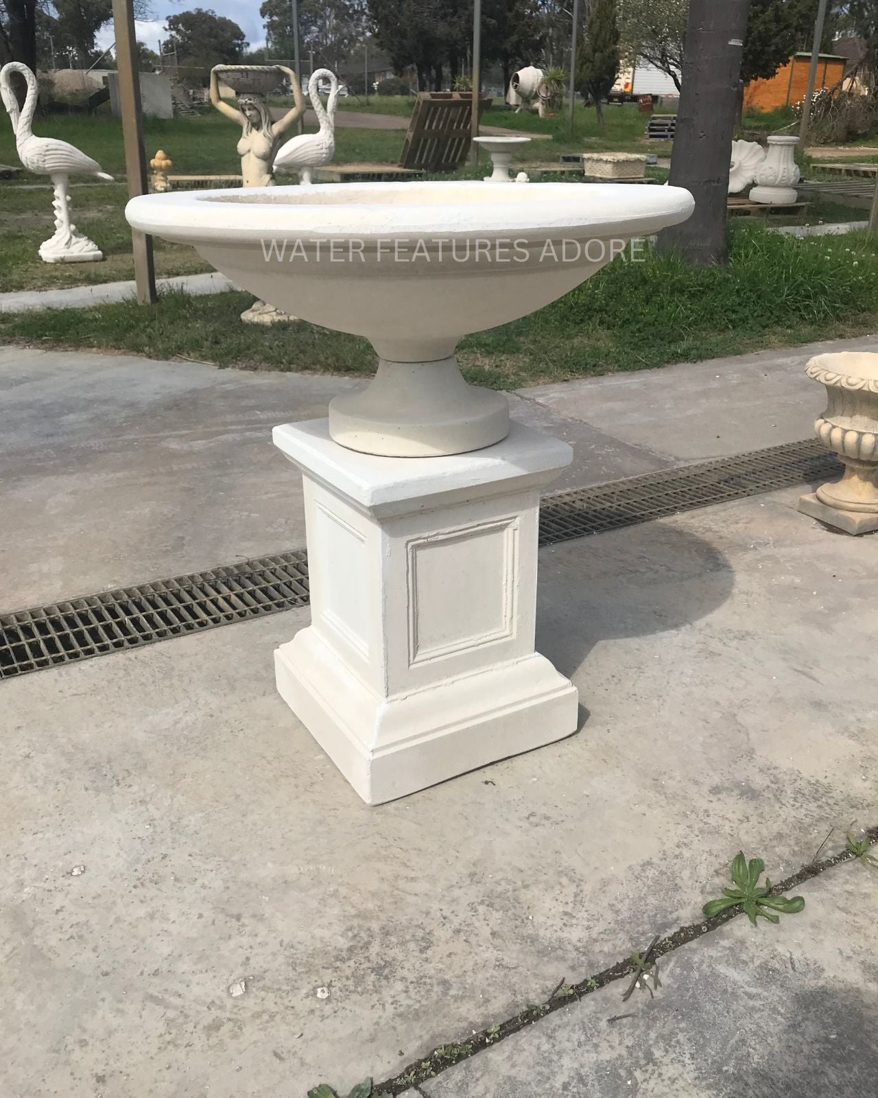Classic concrete bird bath pedestal water fountain in garden setting